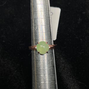 May include: A green gemstone ring set in rose gold with small diamonds on the band.