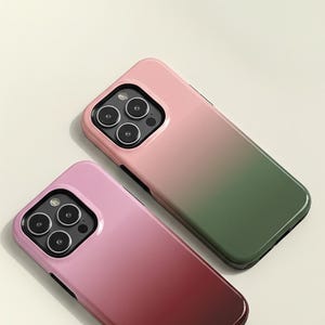 May include: Two smartphone cases with a gradient design. One case transitions from pink to green, and the other from pink to burgundy. Both cases have a glossy finish and a black border around the camera.