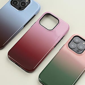 May include: Three smartphone cases in a gradient color scheme. The cases are in shades of blue to brown, pink to red, and pink to green. The cases have a glossy finish and a camera cutout.