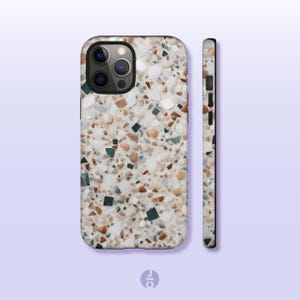 Peut inclure: Une coque de téléphone iPhone blanche avec un motif terrazzo composé de taches brunes, beiges et vertes. La coque a un découpage d'appareil photo noir et un côté noir.