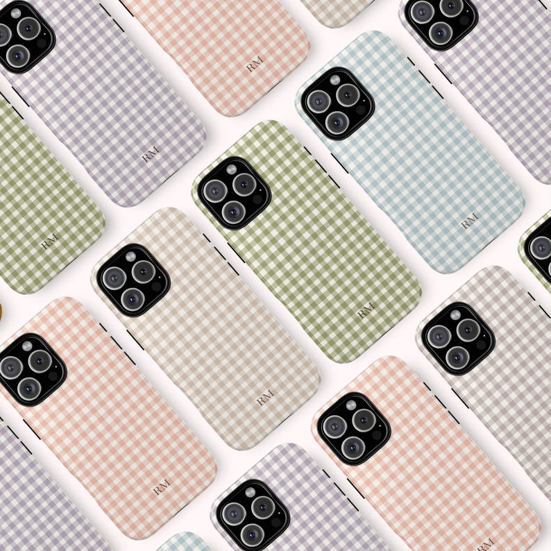 May include: A collection of phone cases in various pastel colors, including lavender, pink, green, beige, and blue. Each case features a gingham pattern and the initials "RM" printed in the lower center. The cases are arranged on a white surface.