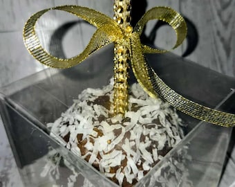 Peut inclure: Une pomme enrobée de chocolat et recouverte de flocons de noix de coco râpée, dotée d'un bâtonnet incrusté de strass dorés et d'un ruban métallique doré noué, le tout présenté dans une boîte de présentation carrée en plastique transparent.