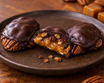Peut inclure: Trois bouchées au chocolat, aux noix de pécan et au caramel sur une assiette brun foncé. La bouchée centrale est coupée en deux, révélant un cœur de caramel ambré doré parsemé de noix de pécan hachées, le tout enrobé d'une coque en chocolat noir.