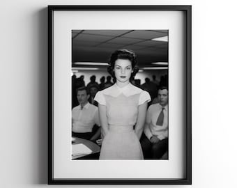 Può includere: Fotografia in bianco e nero di una donna con un vestito in piedi di fronte a un gruppo di persone. La donna guarda direttamente la telecamera. La foto è incorniciata in una cornice nera.