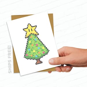 May include: A pixelated Christmas tree card with a green tree, a yellow star on top, and colorful ornaments. The card has the text "SHIPS FREE!" on the left side.