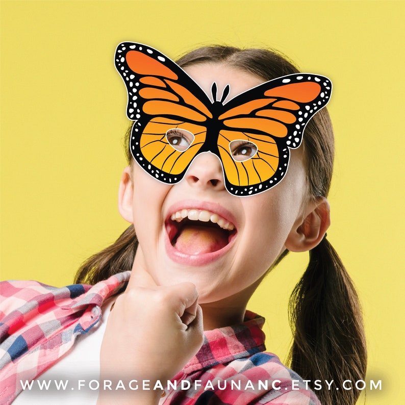 May include: A child wearing a paper butterfly mask with orange and black wings. The mask has eye holes and is held in place with a string. The child is smiling and looking to the side.