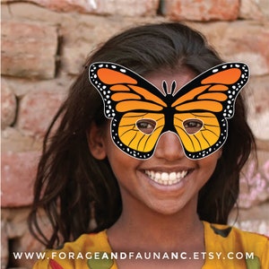May include: A young person wearing a bright orange and black butterfly mask with white polka dots. The mask has eye holes and covers the person's eyes. The person is smiling and has a happy expression.