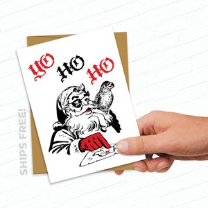 May include: A Christmas card featuring a cartoon illustration of Santa Claus wearing sunglasses and a pirate eye patch. He is holding a map and pointing with his gloved hand. A parrot is perched on his shoulder. The text "YO HO HO" is written in red at the top of the card.