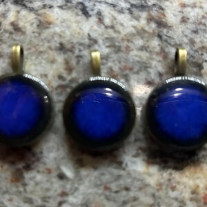 May include: Three round glass pendants with a dark blue center and a black rim. Each pendant has a gold-colored metal bail.