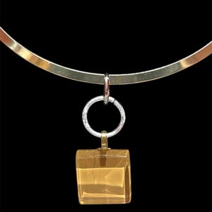 May include: A gold-toned choker necklace with a square, amber-colored pendant. The pendant is suspended from a silver ring and a small gold bail. The necklace has a simple, elegant design, perfect for everyday wear.