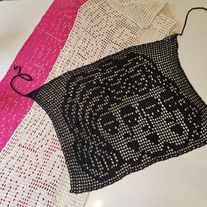 May include: A collection of three crocheted items in shades of pink, cream, and black. The pink and cream pieces are long, rectangular shawls. The black piece is a square-shaped top with a halter neck tie.