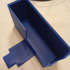 Könnte beinhalten: Ein blauer Plastik-Organizer mit rechteckiger Basis und einem hohen, offenen Fach. Der Organizer hat eine kleine, flache Plattform, die an der Basis befestigt ist.