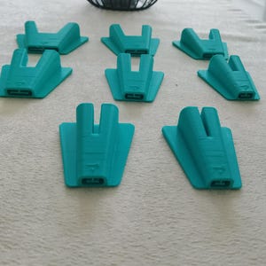 May include: A collection of nine teal-colored, 3D-printed objects. Each object has a rectangular base with two vertical, parallel posts. The objects are arranged on a white surface.