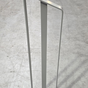 Może przedstawiać: Metalowa poręcz w kolorze szarym z pionowym wspornikiem i ukośnym górnym prętem. Poręcz jest zamontowana na betonowej podłodze.