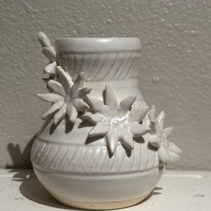 May include: White ceramic vase with a textured surface and three dimensional flower embellishments.