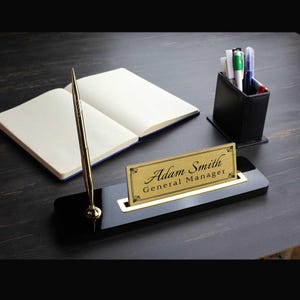 May include: Black desk organizer with a gold nameplate that reads "Adam Smith General Manager" and a gold pen holder.