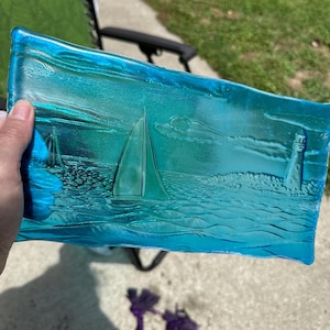 May include: A light blue glass tray with an etched design of sailboats and a lighthouse on a wavy sea.