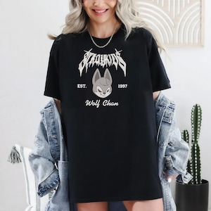 May include: Black t-shirt featuring the text "Stray Kids" in a stylized font above a cartoon wolf face. The text "EST. 1997" and "Wolf Chan" are also printed on the shirt. The shirt is worn with a denim jacket.