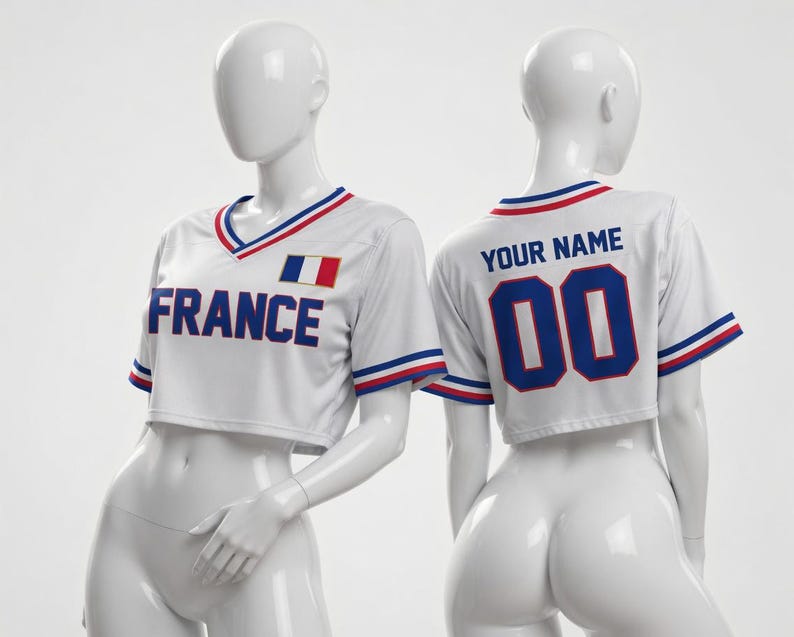 Puede incluir: Camiseta corta blanca con ribetes azules, rojos y blancos. La parte delantera muestra "FRANCE" en letras azules y una bandera francesa. La parte trasera presenta "YOUR NAME" encima del n&uacute;mero "00" en azul.