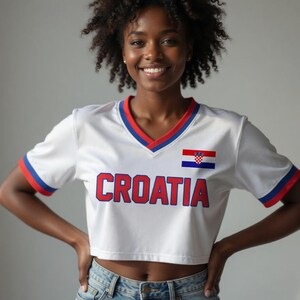 May include: White crop top with red and blue trim, featuring the word "CROATIA" in red block letters and a Croatian flag emblem. The shirt has a V-neck and short sleeves.
