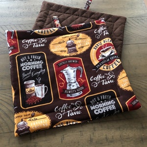 May include: Two brown quilted pot holders with a coffee theme. The pot holders feature a variety of coffee-related designs, including coffee beans, coffee cups, and coffee makers. The text on the pot holders includes "Coffee Time", "Hot & Fresh Morning Coffee", "Locally Brewed", "Premium Quality Coffee", and "House Blend".