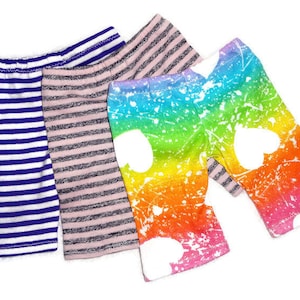 Peut inclure: Quatre paires de leggings pour enfants aux motifs variés. Une paire est à rayures bleues et blanches, une autre à rayures roses et grises, et une troisième est arc-en-ciel avec des cœurs blancs. La quatrième paire est rayée.