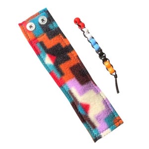 May include: A colorful patterned fleece wrist strap with two snap buttons and a beaded string with red, white, blue, black, and orange beads.