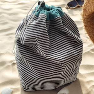 May include: A striped drawstring bag with a teal lining. The bag is made of a soft, cotton fabric and is ideal for carrying beach essentials.