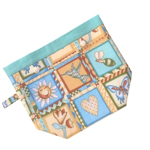 Peut inclure: Une pochette en tissu bleu et jaune avec un motif patchwork représentant un colibri, un papillon, un tournesol, un cœur et une tulipe. La pochette est ornée d'une bordure rayée verte et bleue et d'une fermeture à bouton.