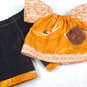 May include: A doll's outfit comprising dark blue denim-style trousers and an orange top. The top has a brown pocket and is decorated with patterned trim and sleeves. The outfit is designed for a doll.