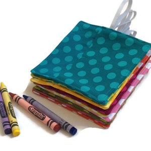 May include: A stack of colorful fabric squares with polka dot patterns. The squares are folded and stacked, with the top square being teal with white polka dots. There are crayons in the foreground.