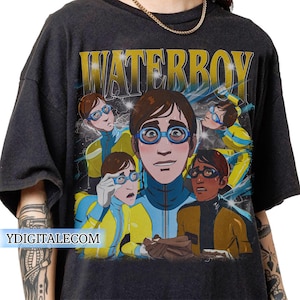 May include: Dark gray t-shirt featuring a graphic of a cartoon character with blue glasses and a yellow and blue outfit. The word "WATERBOY" is printed in gold letters above the graphic. The website "YDIGITALECOM" is printed at the bottom.