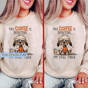 Può includere: Una felpa beige con la scritta "THIS COFFEE IS DEFECTIVE, I'M STILL TIRED." presenta un cane dei cartoni animati con un'espressione triste. Il cane indossa una maglietta arancione ed è seduto accanto a una tazza di caffè.