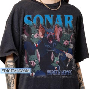 May include: Dark gray t-shirt featuring a graphic of bat-like creatures in suits with the word "SONAR" in blue above them. The text "DISPATCH HEROES" is below the graphic. The website "YDIGITALECOM" is printed on the left side.