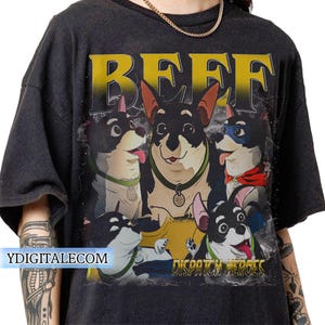 Puede incluir: Camiseta gris oscuro con un gráfico de corgis de dibujos animados y la palabra "BEEF" en letras amarillas. La frase "DISPATCH HEROES" está debajo de los corgis. El sitio web "YDIGITALECOM" está impreso en la parte inferior izquierda.
