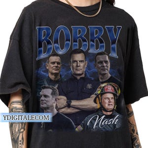 Può includere: T-shirt nera con grafica di un uomo e il nome "Bobby" in blu. Il design include più immagini dello stesso uomo in pose diverse, con il nome "Nash" sotto.