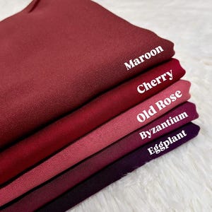 May include: A stack of five fabric swatches in shades of red, pink, and purple. The swatches are labeled from top to bottom: Maroon, Cherry, Old Rose, Byzantium, and Eggplant.