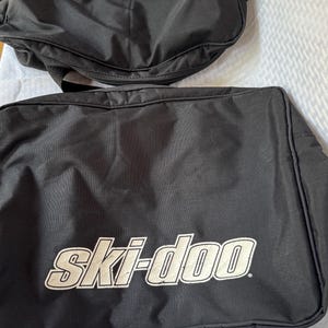 May include: Two black Ski-Doo branded bags. The larger bag has the words "ski-doo" in white block letters. The smaller bag has the words "doo-ski" in white block letters. Both bags are made of a durable material.