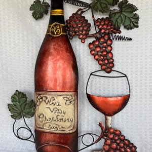 May include: A metal wine-themed wall art piece featuring a wine bottle, a glass of wine, and grape clusters. The bottle has a label that reads "Wine Valley Chardonnay 2005". The art piece is painted in shades of red, green, and gold.
