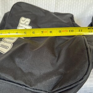 May include: Black duffel bag with the word "Davis" in white lettering. The bag is measured with a yellow tape measure, showing a length of approximately 13 inches.