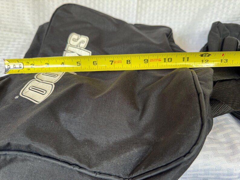 May include: Black duffel bag with the word "Davis" in white lettering. The bag is measured with a yellow tape measure, showing a length of approximately 13 inches.