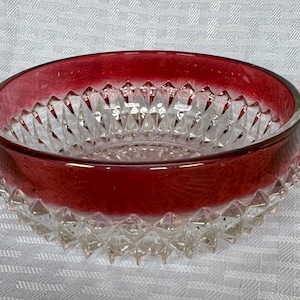 May include: A clear glass bowl with a ruby red rim and a diamond-cut pattern. The bowl's exterior has a textured, spiky design. The bowl is likely used for serving or display.