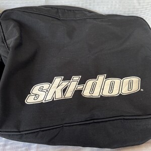 May include: Black bag with the white text "ski-doo" in a stylized font. The bag appears to be made of a durable material and is likely designed for carrying equipment. The bag is rectangular and has a simple design.