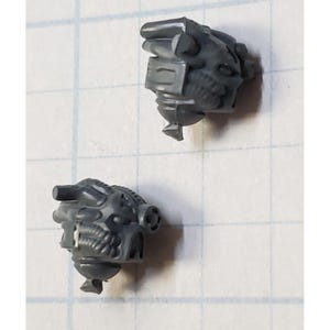 May include: Two gray plastic miniature heads with intricate details, resembling futuristic helmets or robot heads.