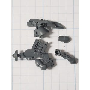 May include: A set of gray plastic miniature parts for a model kit. The parts include a gun, a hand, and a shoulder piece.