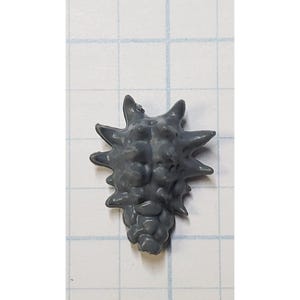 May include: A small, gray, spiky object with a textured surface. The object has a rounded base and multiple pointed protrusions radiating outwards. The object is set against a grid background.