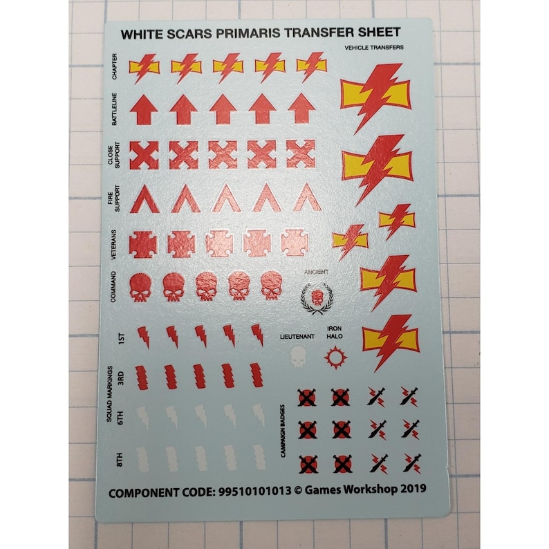 May include: A sheet of White Scars Primaris transfer decals. The sheet features various red and yellow vehicle transfers, including arrows, lightning bolts, skulls, and campaign badges. Text includes "Chapter", "Battleline", "Close Support", and "Squad Markings".