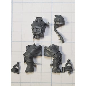May include: Gray plastic miniature parts for a model kit. The parts include a torso, two legs, a helmet, and two small accessories.