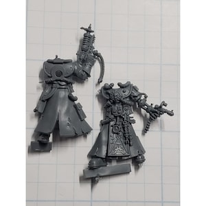 May include: Two unpainted plastic miniature figures. One figure is a torso with a long coat and a backpack. The other figure is a torso with mechanical details, a long coat, and a weapon. The figures are gray.