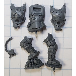 May include: Gray plastic miniature parts for a model kit. The parts include a torso, two legs, two arms, and a head. The parts are designed to be assembled together to create a complete model.